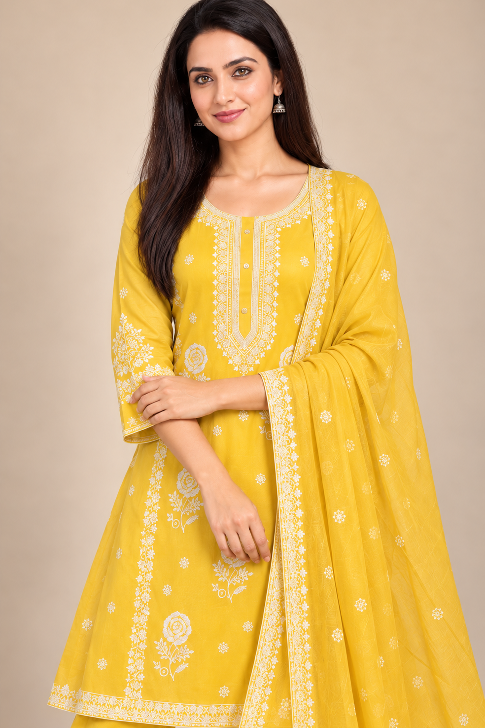 A woman modeling a yellow traditional Indian salwar kameez suit with white embroidery, featuring a matching dupatta, set against a solid beige background.