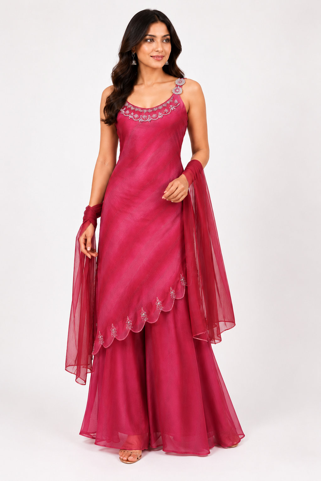 A woman modeling a magenta pink traditional Indian outfit consisting of a sleeveless kurta with silver embroidery, matching flared pants, and a sheer dupatta, set against a plain white studio background.