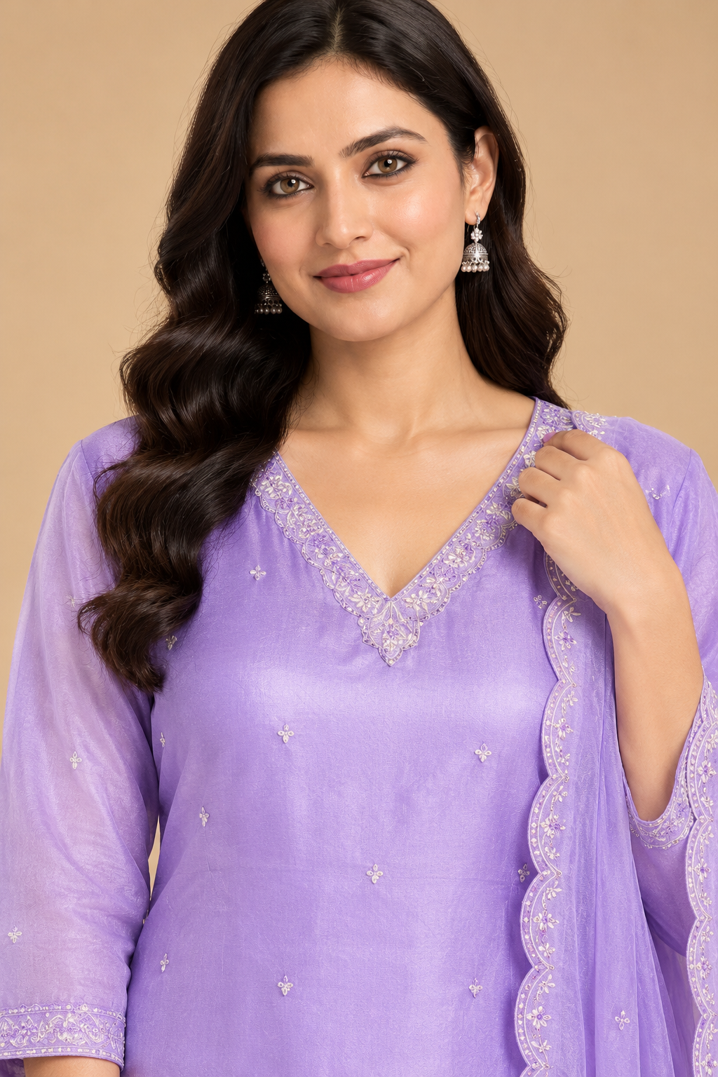 A woman wearing a lavender purple traditional Indian kurta with silver embroidered details and a matching sheer dupatta, set against a solid beige background.