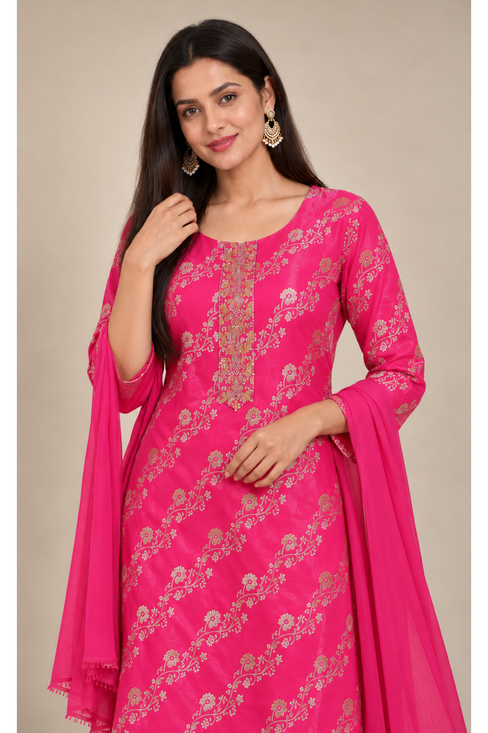 A woman modeling a bright pink traditional Indian salwar kameez set with gold floral embroidery and a matching pink dupatta, set against a plain beige background.